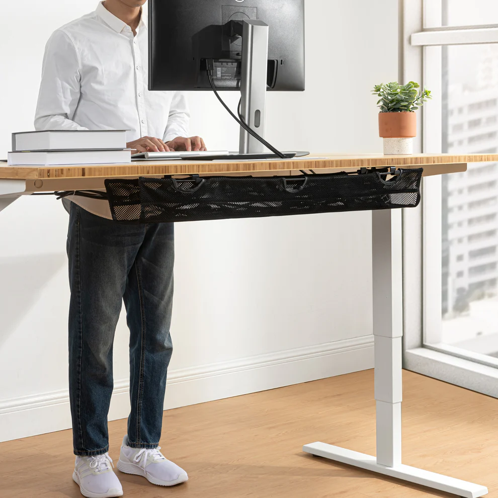 Person standing at a bamboo standing desk with a black mesh cable management tray mounted underneath