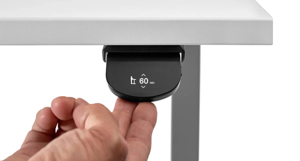 Finger pressing a digital under-desk control panel showing a 60-minute stand-reminder timer